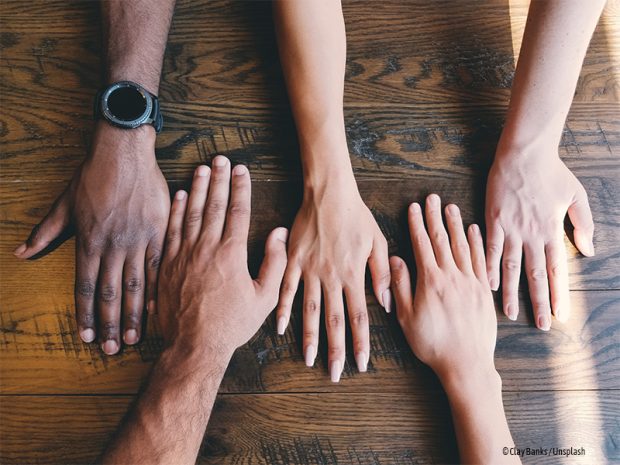 Arme und Hände unterschiedlicher Hautfarben kommen als Symbol für Integration in der Mitte des Bildes nebeneinander zusammen