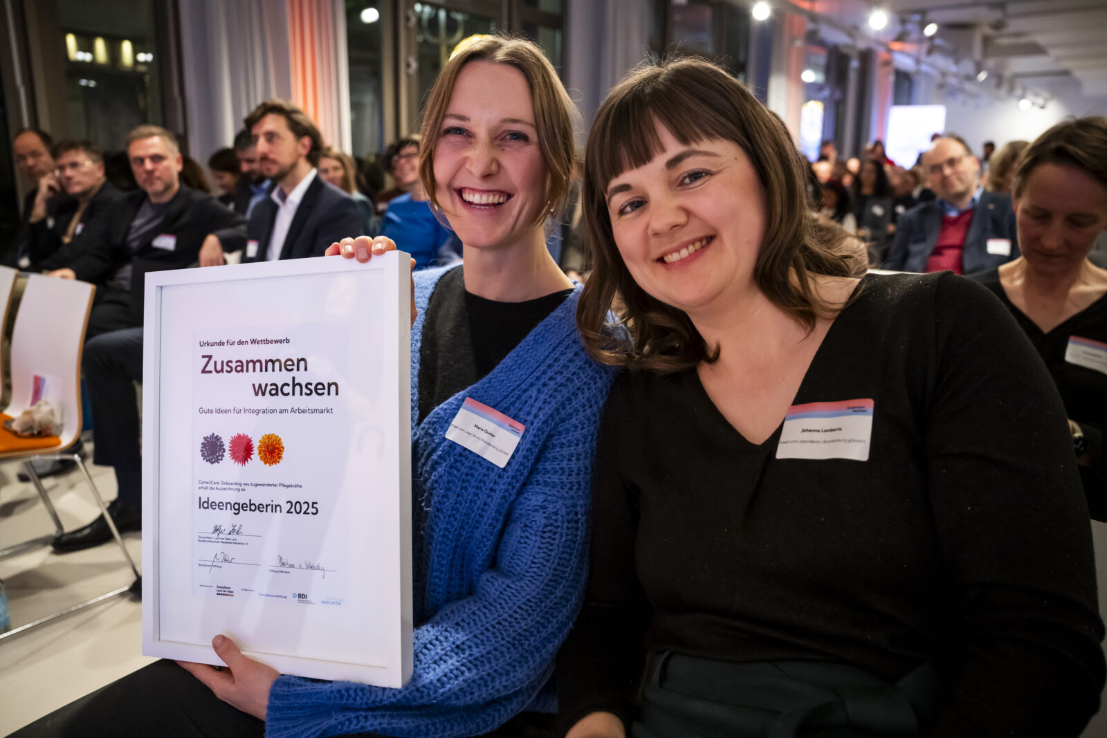 Zwei Vertreterinnen des Projekts Come2Care halten die Urkunde in die Kamera und freuen sich.